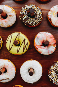 Frosted donuts hang on wooden pegs at a dessert stand. Photo by Anastasiia Chepinska via UnSplash.