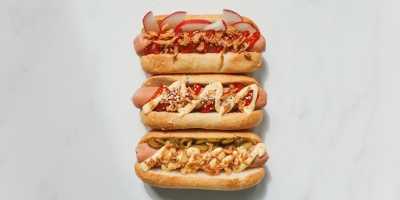 Image of three hot dogs with various toppings on white surface. Photo by Polina Tankilevitch via Pexels.