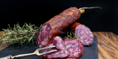 Salami sausage on black chopping board with rosemary and meat fork. Image by Wesual Click via Unsplash.