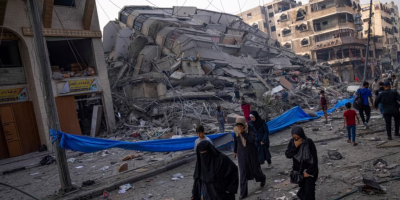 Palestinians walk by the rubble of a building after it was hit by an Israeli airstrike, in Gaza City, Photo via VOA News