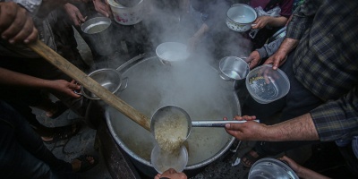 Photo of food being laddled from a large pot, surrounded by hands holding empty bowls in Gaza. Image by Yousef Masoud via Pixabay.