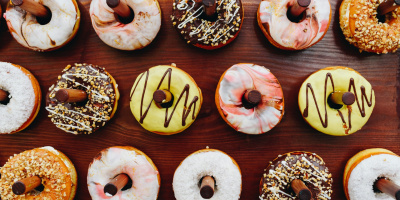 Frosted donuts hang on wooden pegs at a dessert stand. Photo by Anastasiia Chepinska via UnSplash.