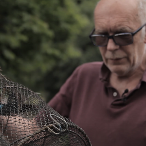 Bob Ring holds a crayfish trap, a black net stretched by a collapsible wire cylinder.