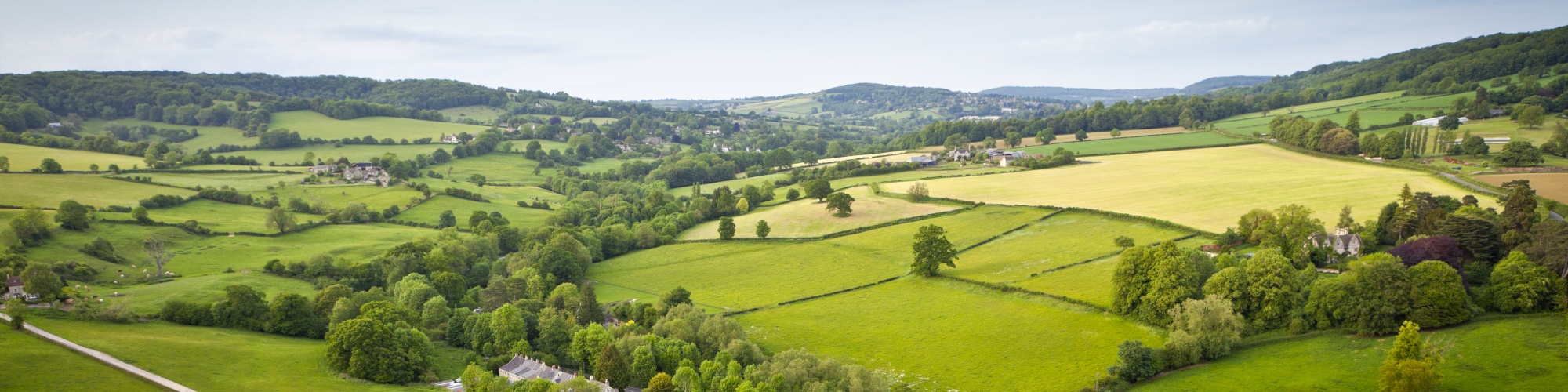 A green valley in the UK with green trees and agricultural lands with a road running through the middle.