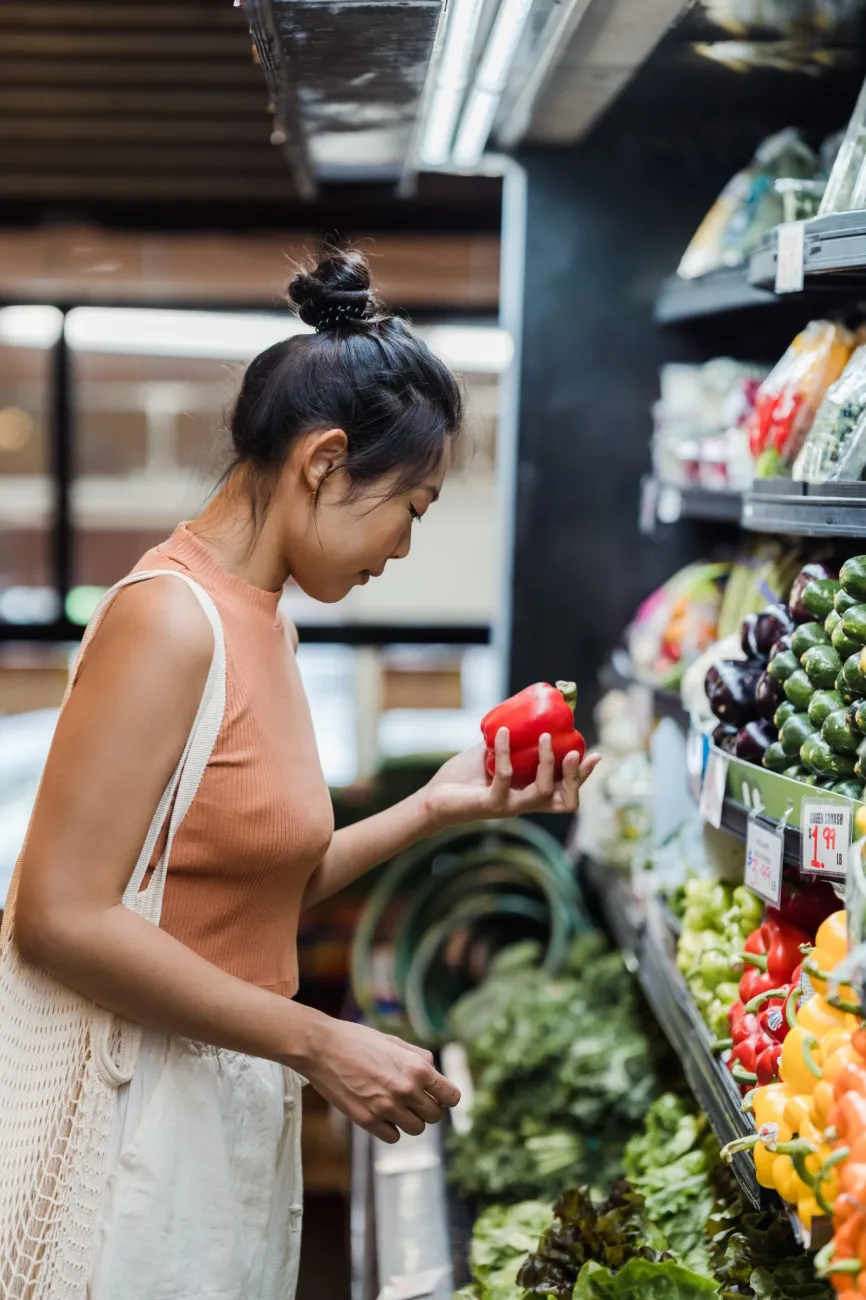 Image of a woman looking at vegetables in a supermarket aisle. Photo by Greta Hoffman via Pexels