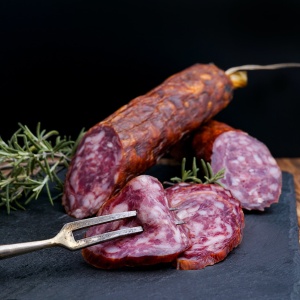 Salami sausage on black chopping board with rosemary and meat fork. Image by Wesual Click via Unsplash.