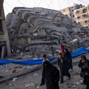 Palestinians walk by the rubble of a building after it was hit by an Israeli airstrike, in Gaza City, Photo via VOA News