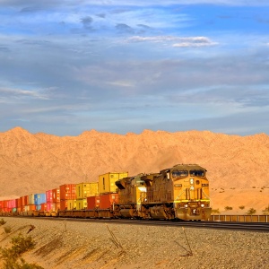 A train carrying many shipping containers through a desert landscape. Photo by jdblack via Pixabay. 